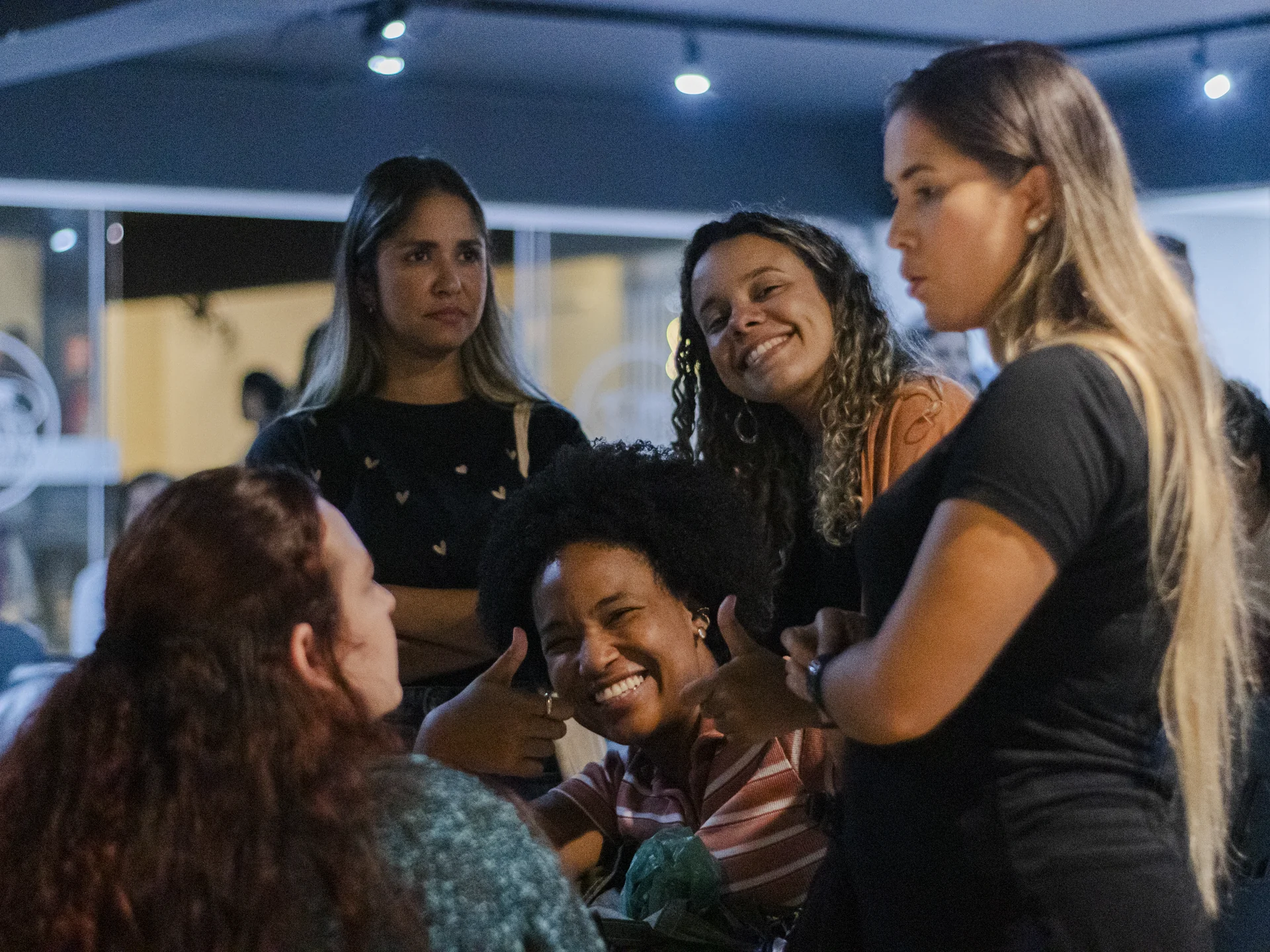 Grupo de mulheres conversando ao redor de uma mesa, com uma participante fazendo sinal de positivo.