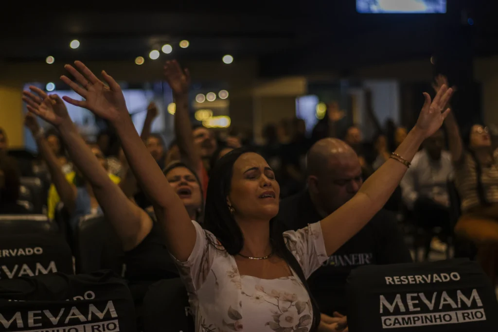 Mulher com as mãos levantadas em meio à comunidade durante um culto.