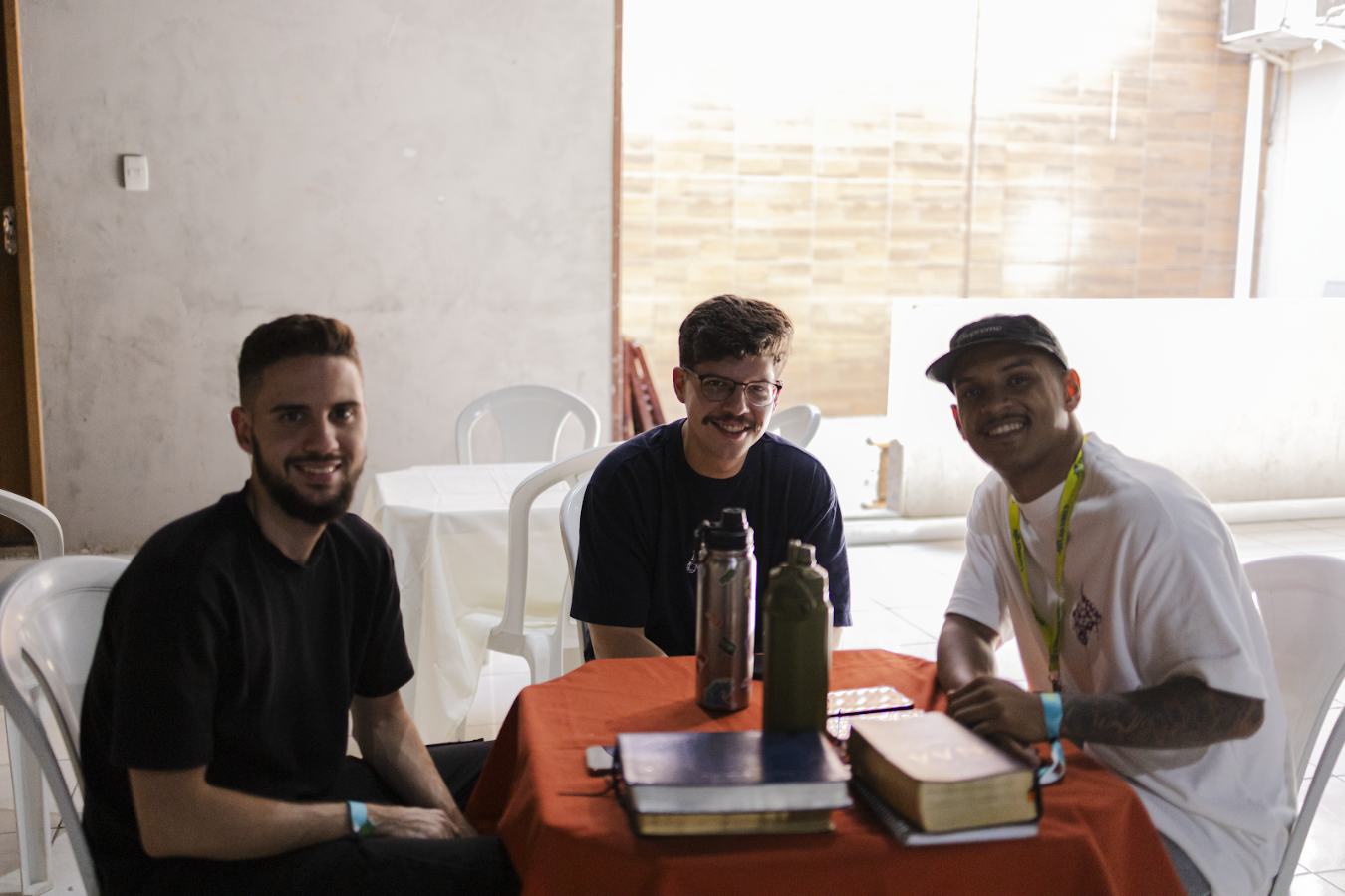Três jovens reunidos à mesa durante o Convergir, com Bíblias e garrafas sobre a mesa.